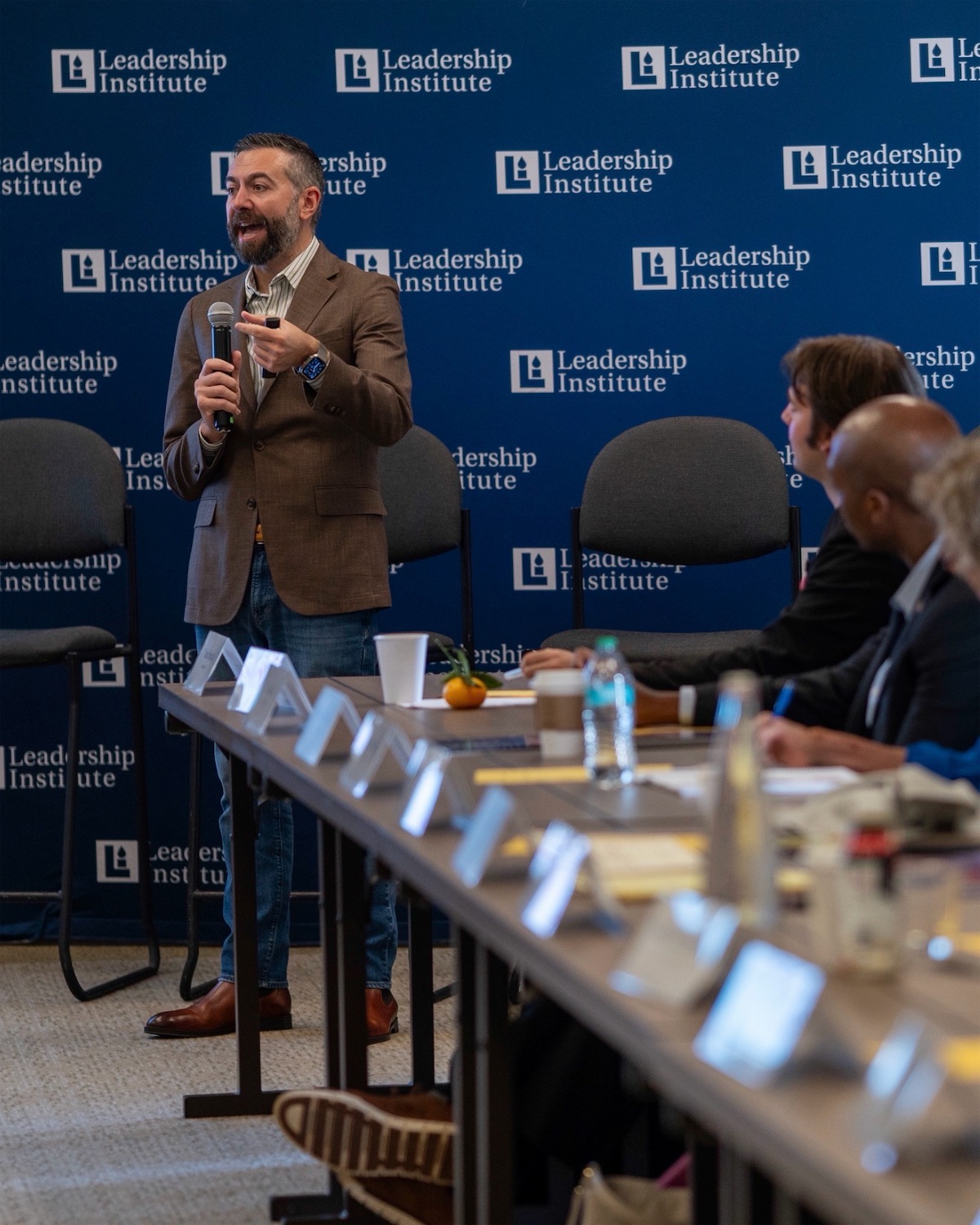 Matt Shupe speaking with a microphone to a seated room in front of a Leadership Institute backdrop