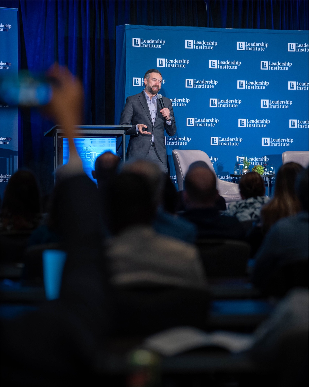 Matt Shupe on stage with a microphone in front of a full audience at a Leadership Institute event