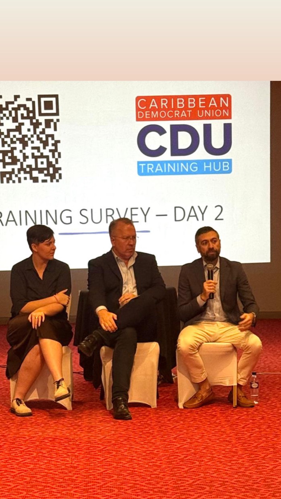 A three-person panel seated before a Caribbean Democrat Union Training Hub screen